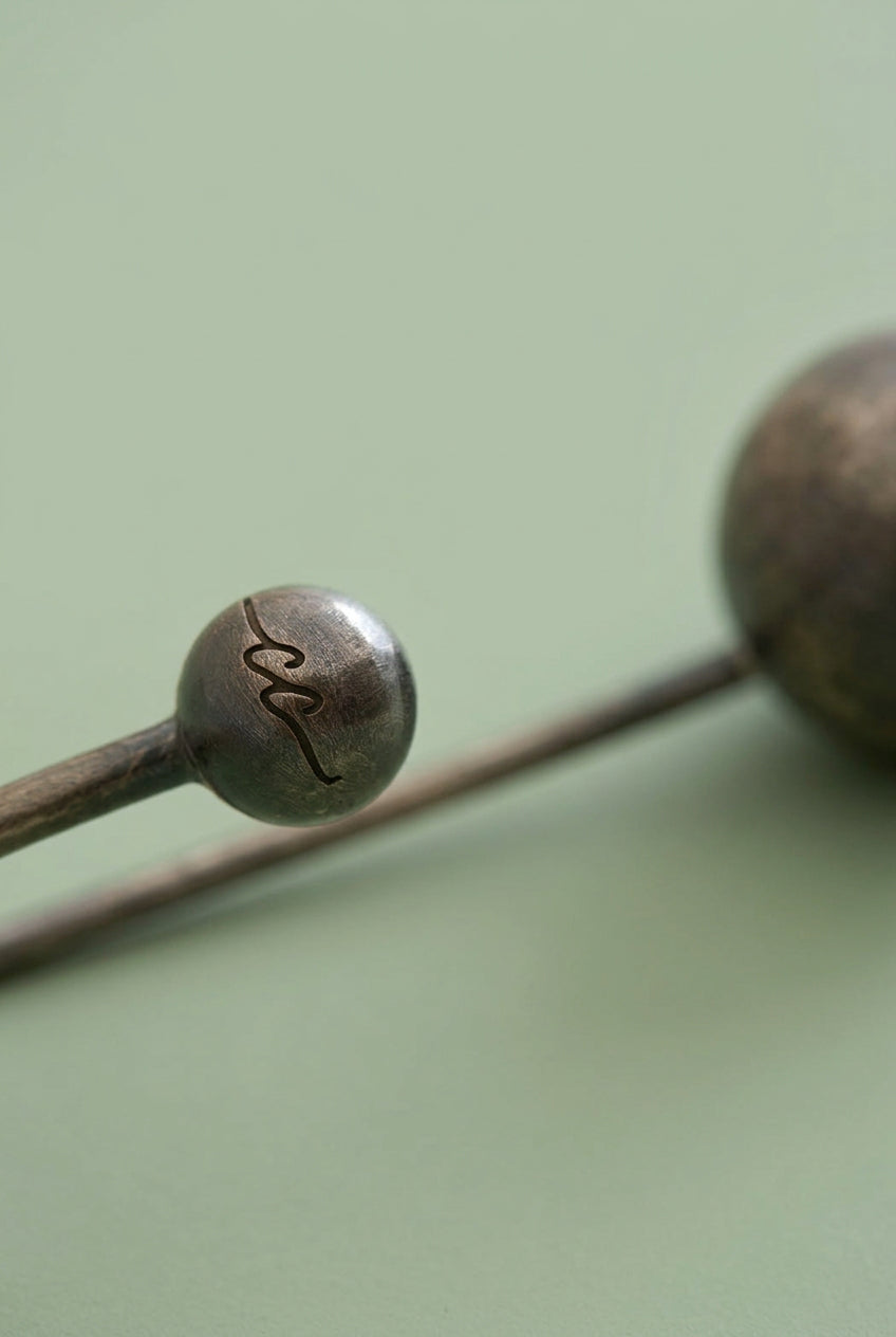 Close-up of a metal hairpin with a signature on a white background