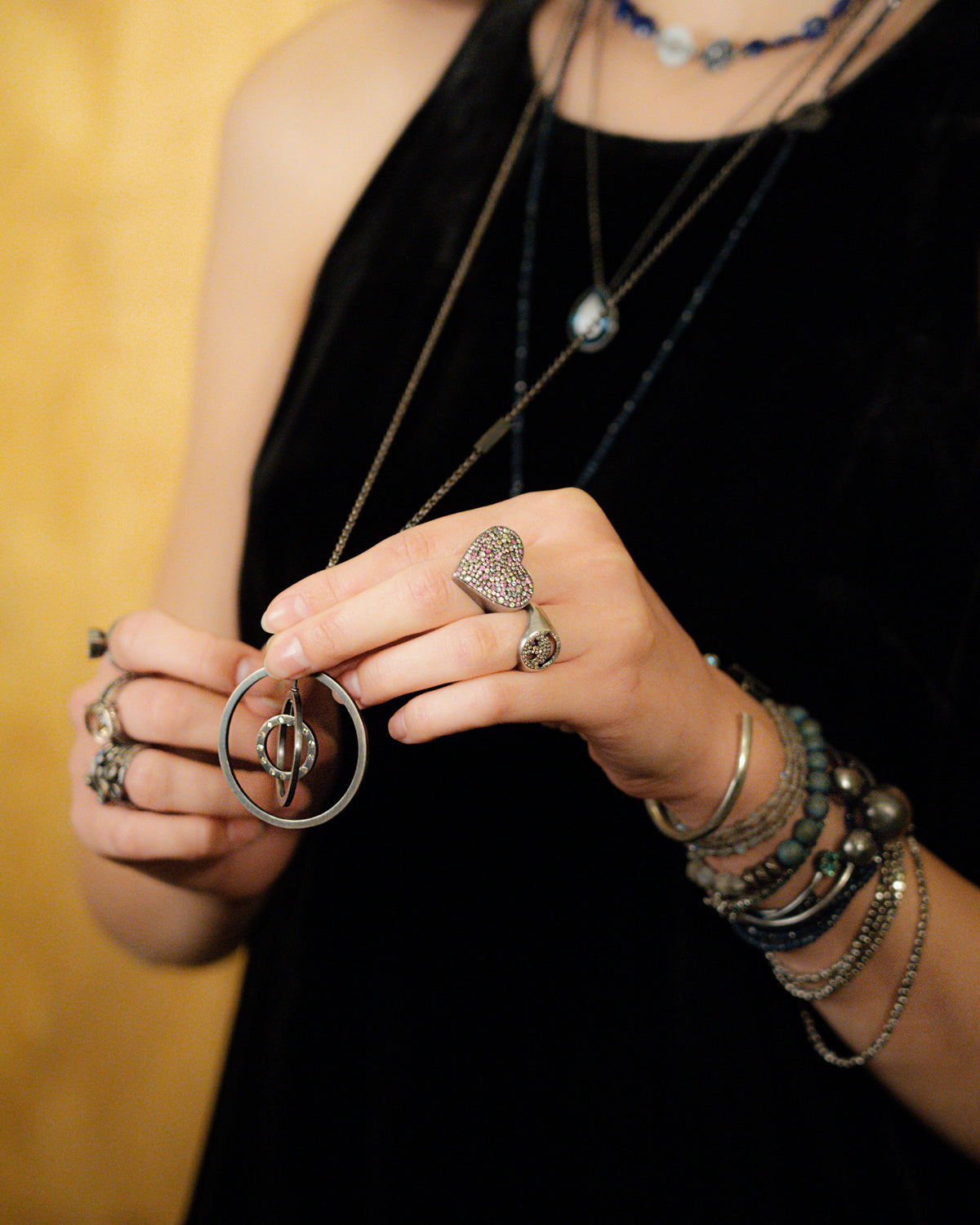 Person wearing multiple necklaces, rings, and bracelets on a blurred background