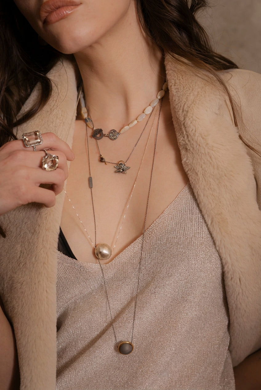 Close-up of a person wearing layered necklaces and rings with a neutral background