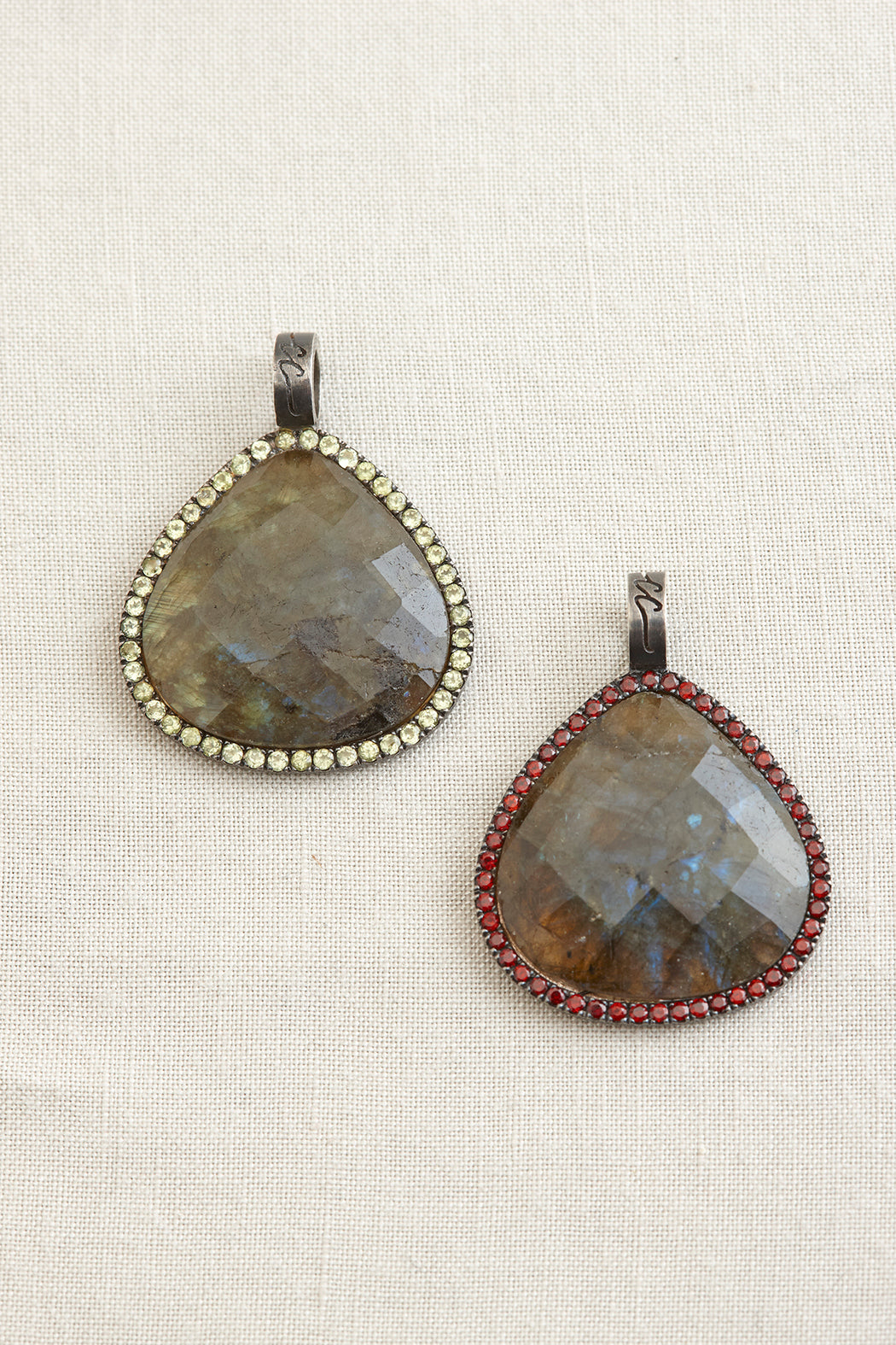 Two labradorite pendants with gemstone accents on a textured white background