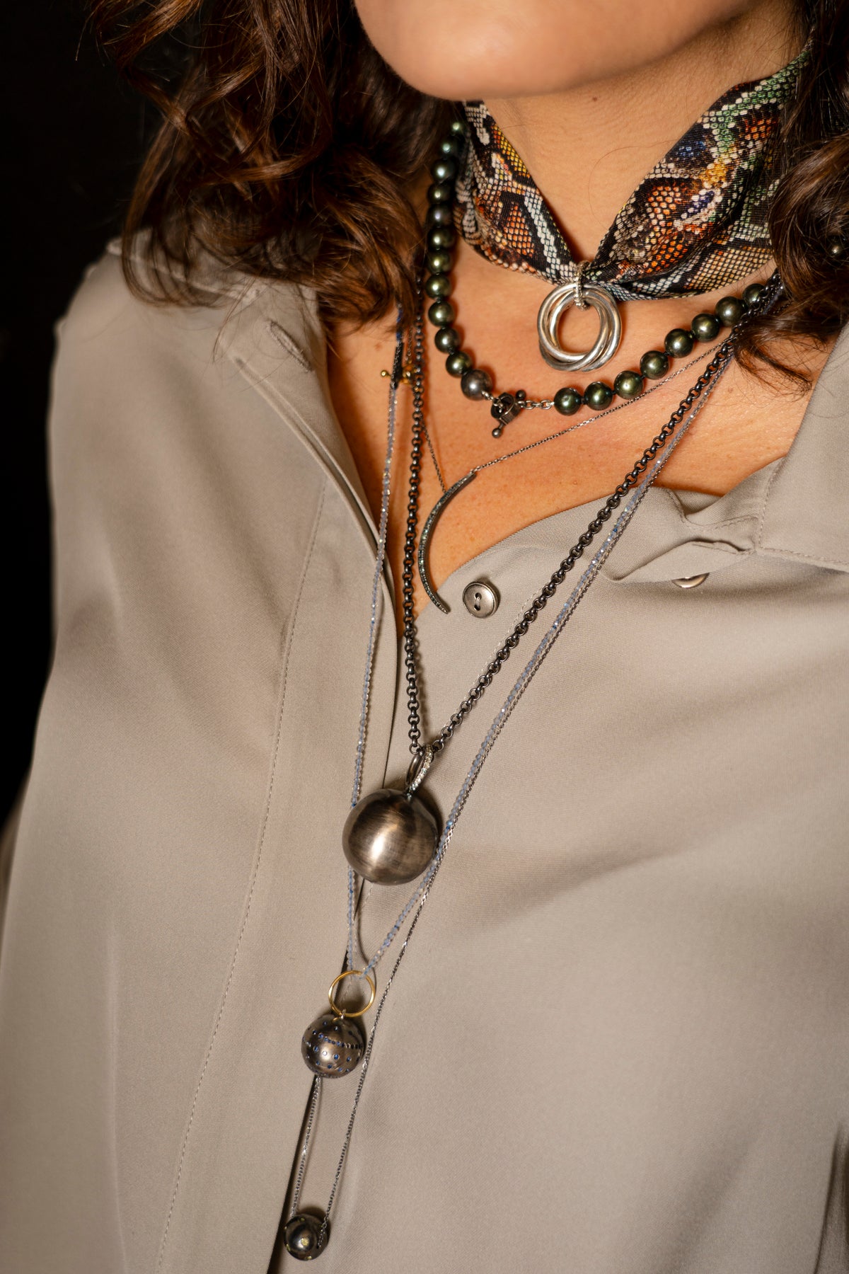 Close-up of a person wearing multiple necklaces with a neutral background