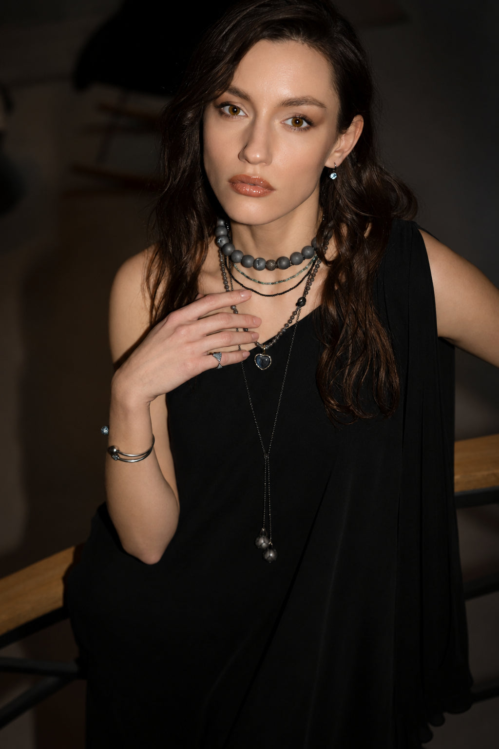 Woman wearing multiple necklaces in a dimly lit setting