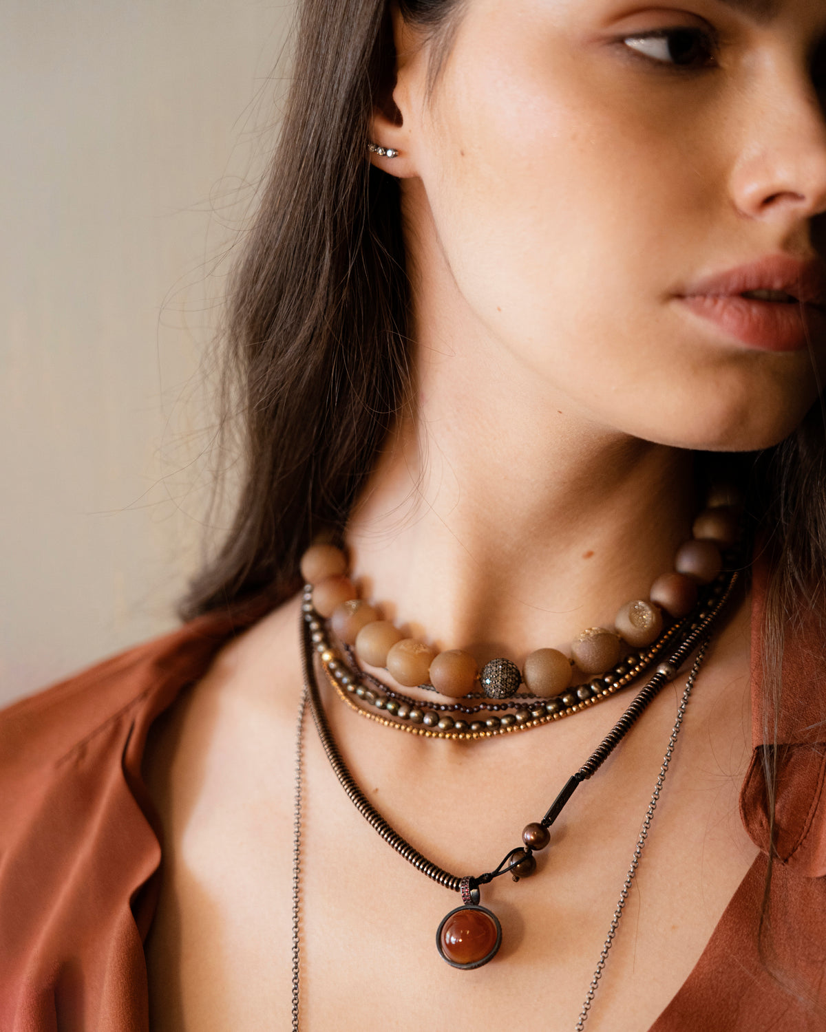 Woman wearing a necklace with brown beads and a pendant against a neutral background