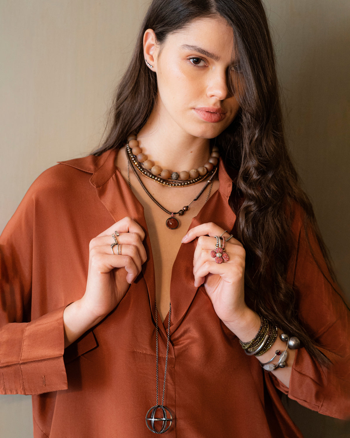 Woman wearing a brown shirt and multiple necklaces with a neutral background