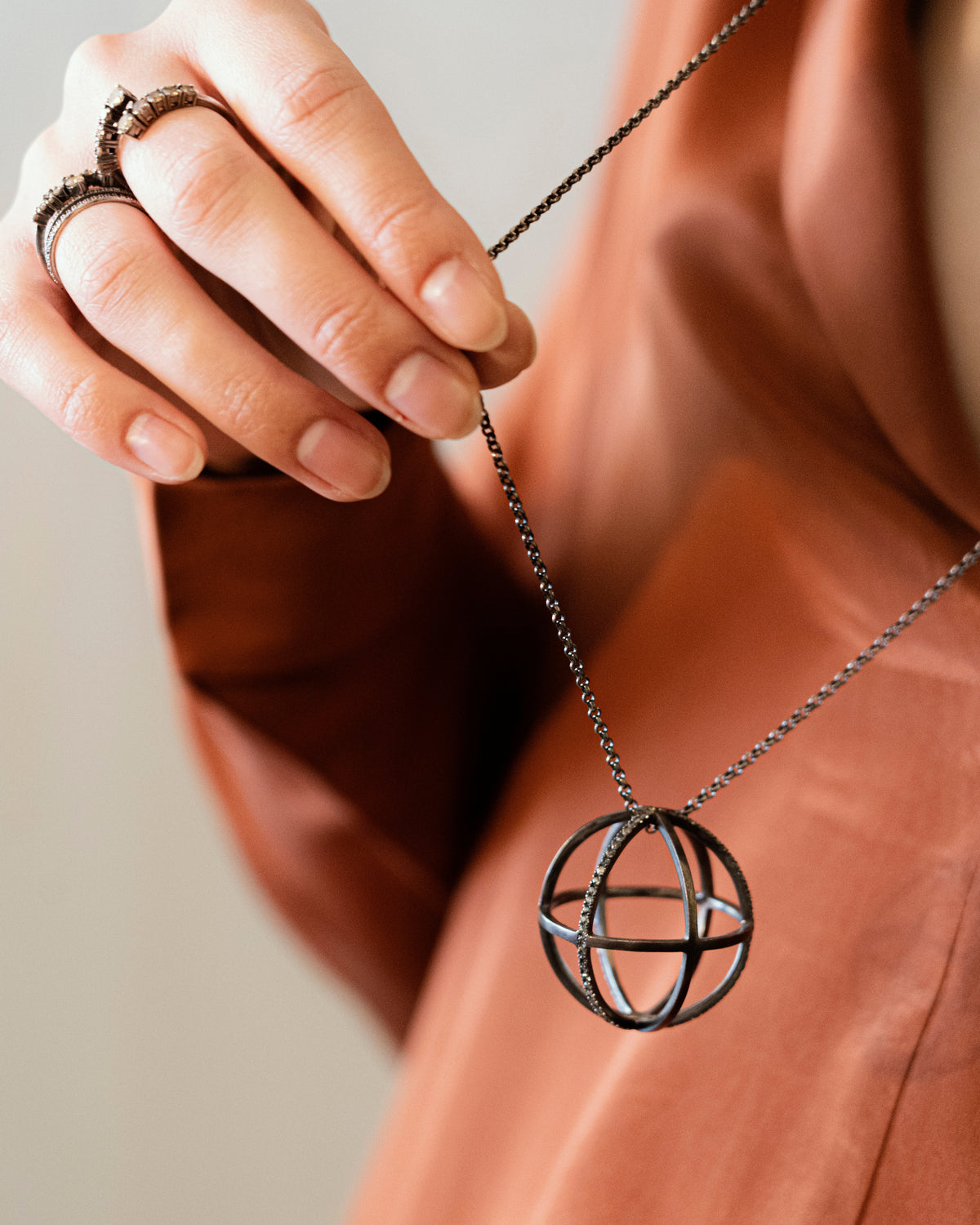 Person wearing a necklace with a spherical pendant on a plain background