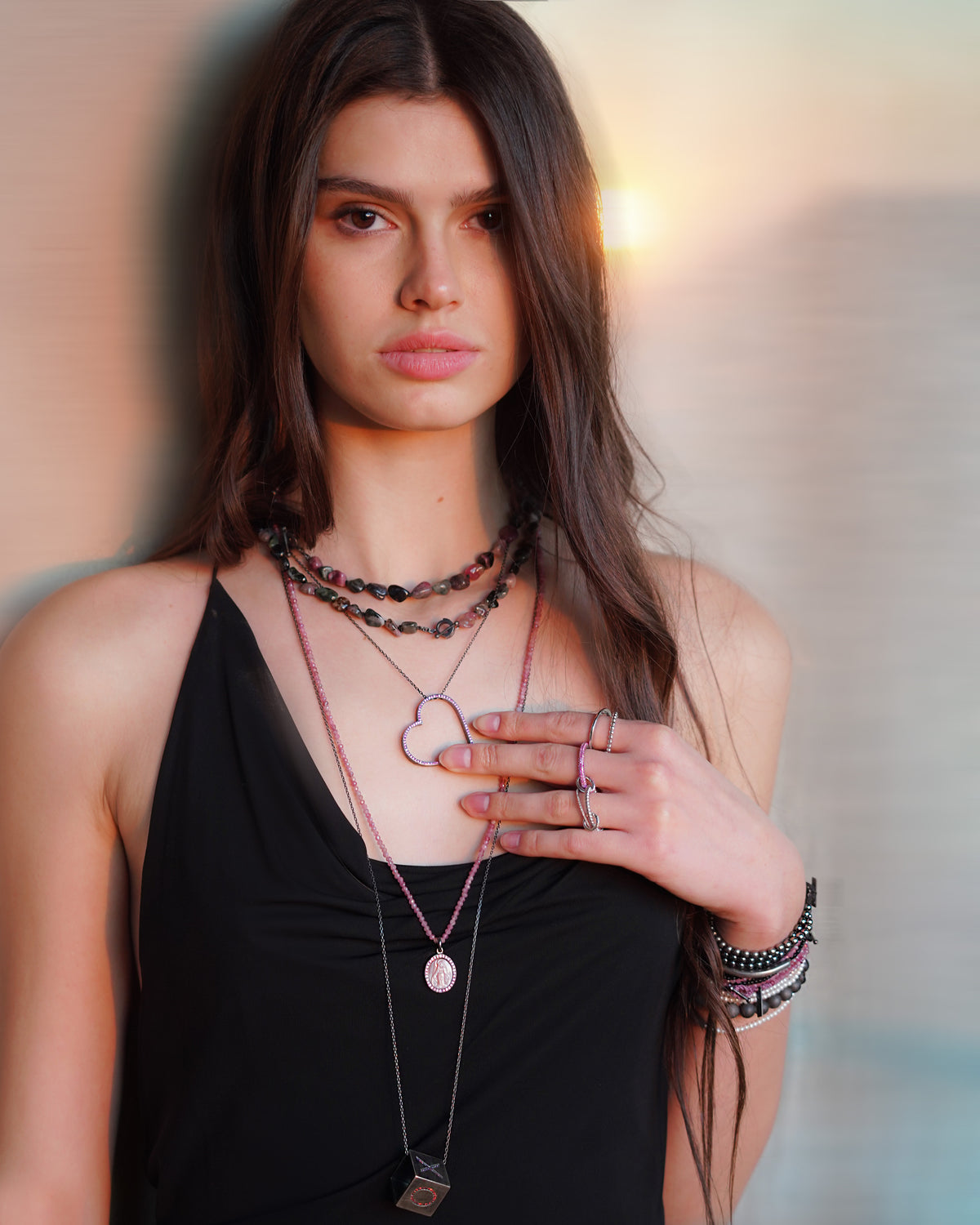 Woman wearing multiple necklaces and bracelets against a neutral background