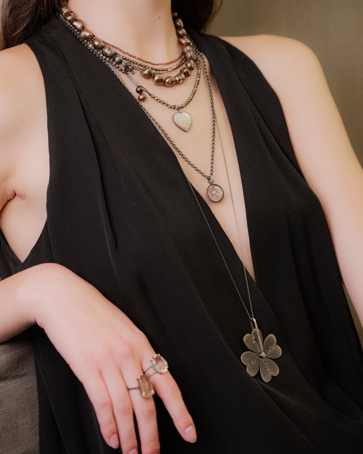 Person wearing layered necklaces and rings with a black sleeveless top.