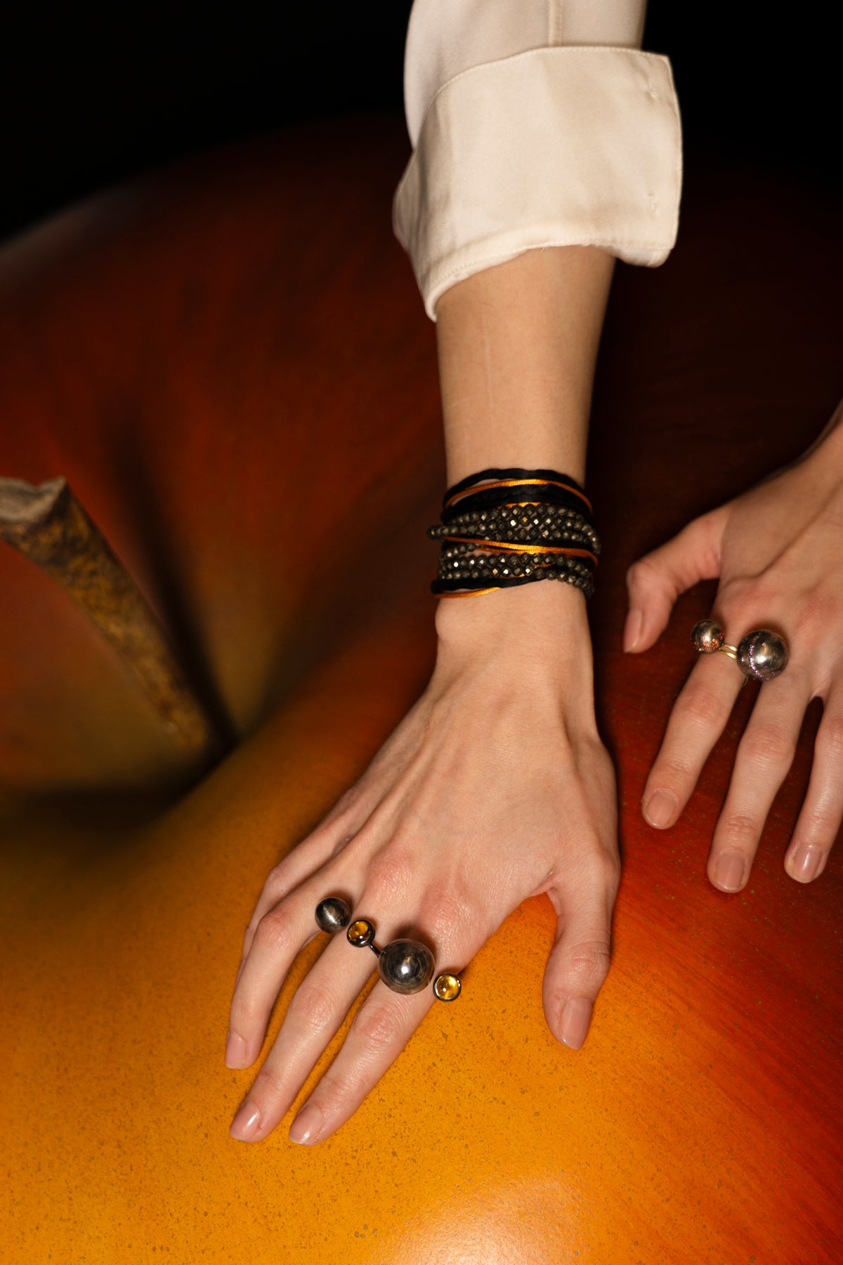 Close-up of a hand wearing multiple rings and bracelets on a wooden surface.