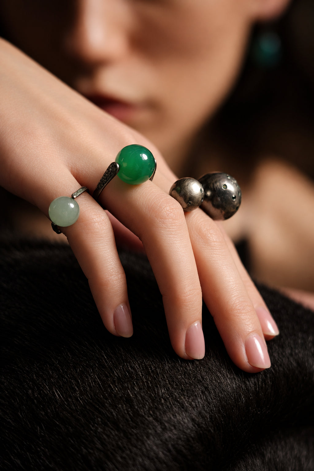 Close-up of a hand wearing multiple rings with green and silver stones on a dark background