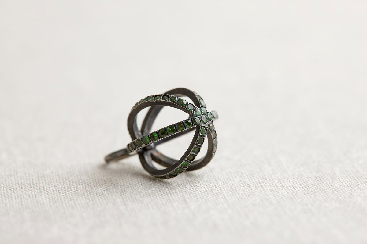 Black ring with green gemstones on a light fabric background
