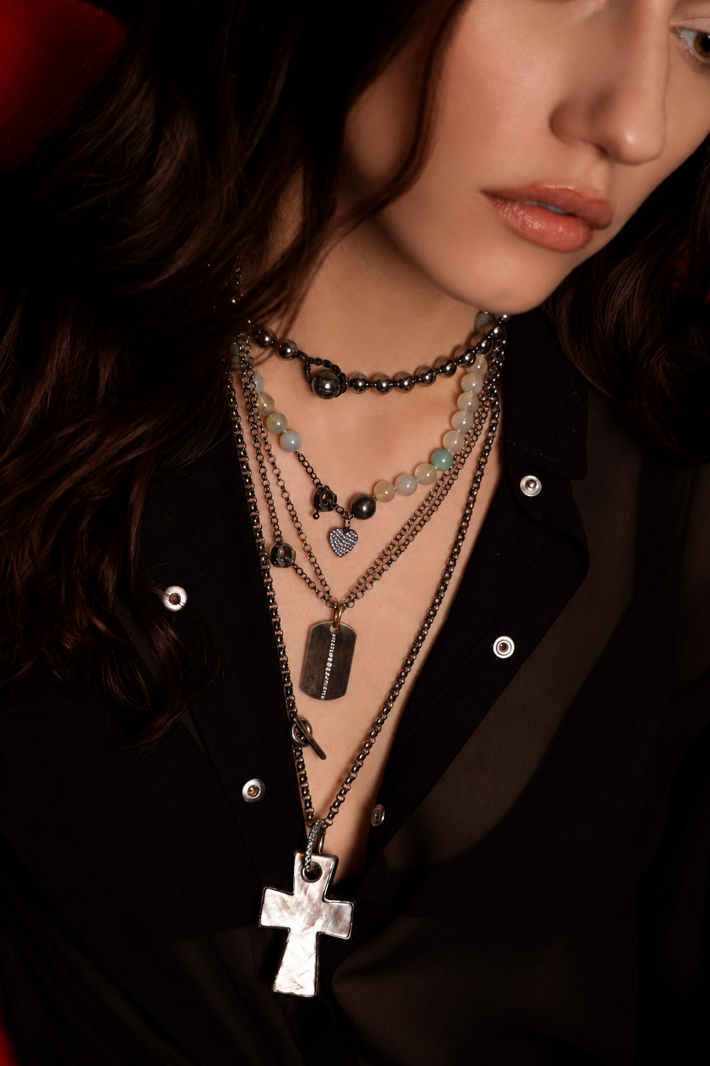 Close-up of a person wearing multiple necklaces with various pendants on a dark background