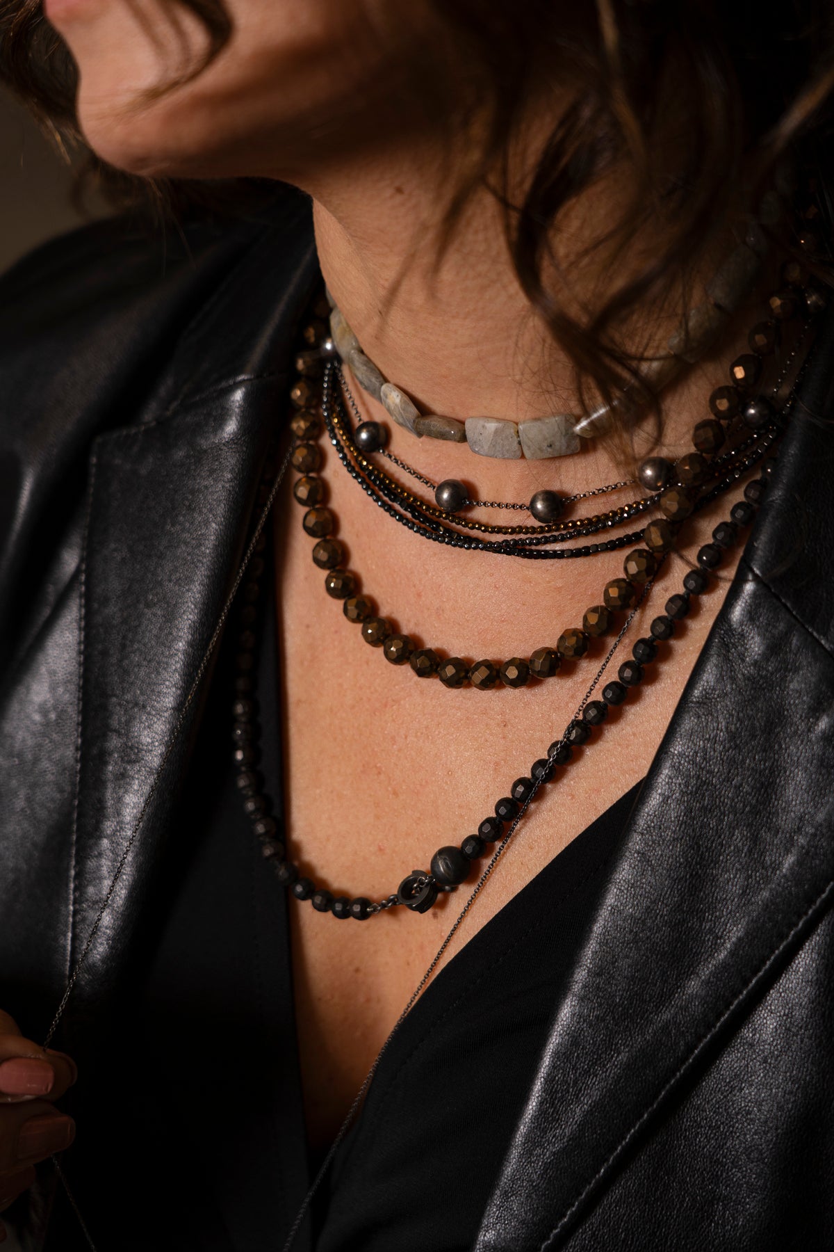 Close-up of a person wearing multiple necklaces with a dark background