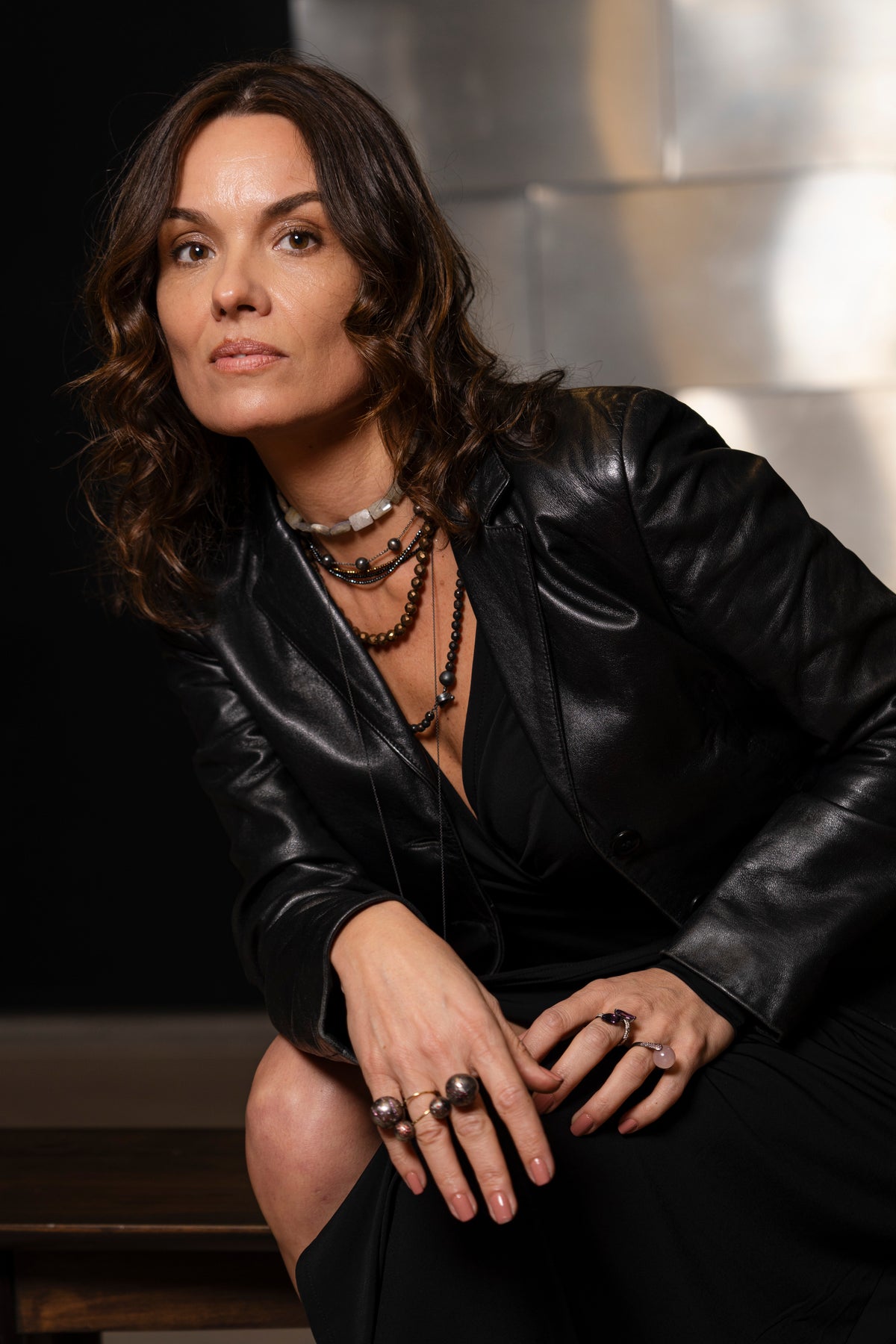 Woman wearing a black leather jacket and multiple necklaces with a dark background
