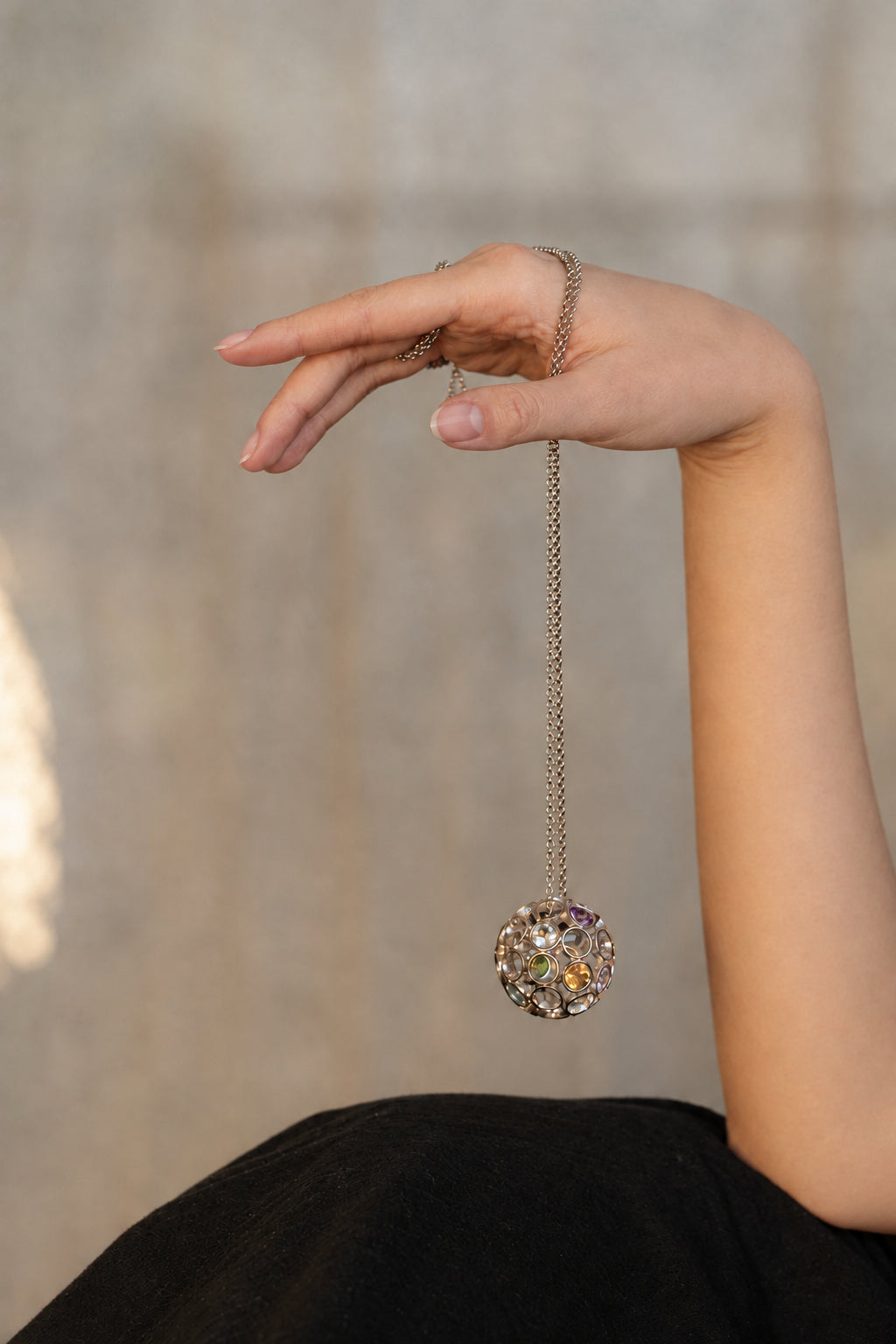 Hand holding a silver necklace with a floral pendant against a blurred background