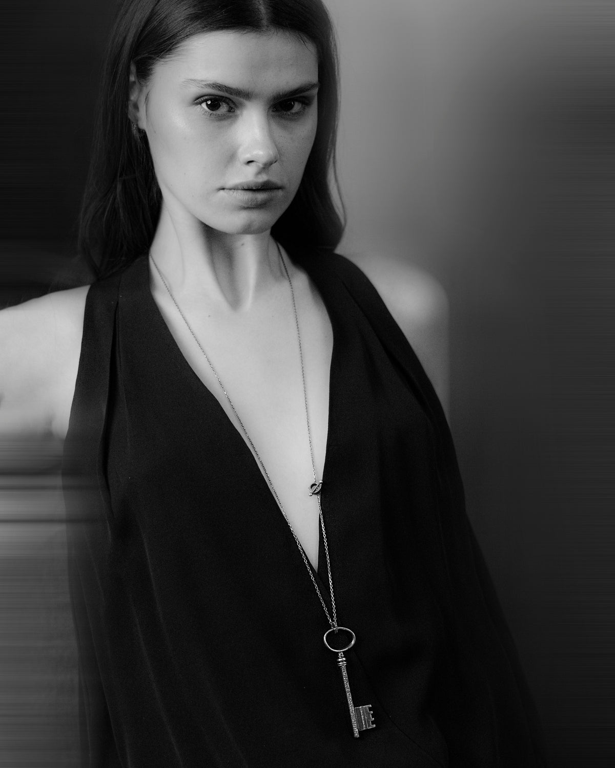 Black and white portrait of a woman wearing a deep neckline top with a key-shaped pendant.