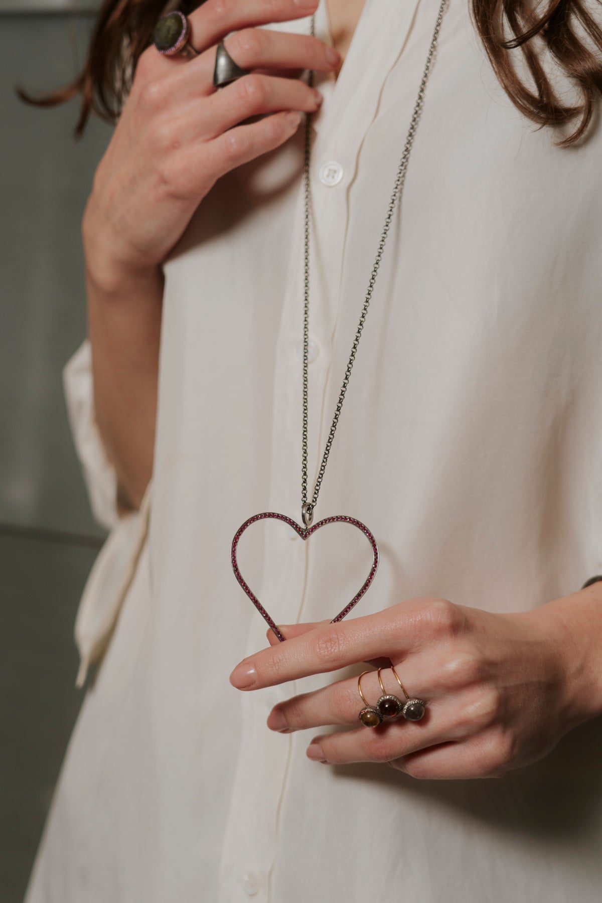 Person wearing a necklace with a heart pendant, holding it close to their chest.