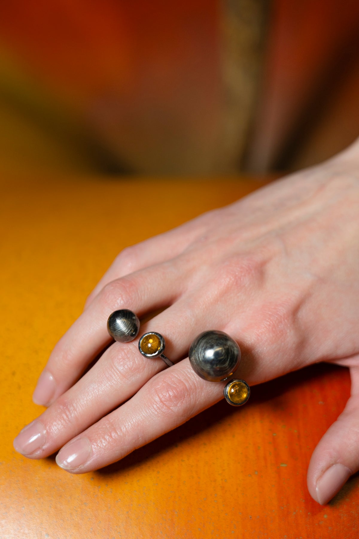 Hand wearing three rings with different colored stones on a wooden surface