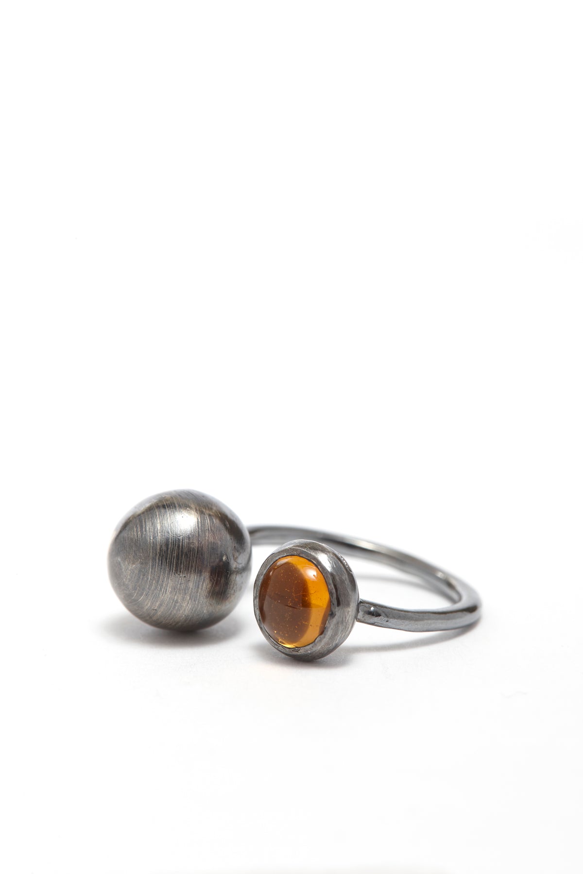 Silver ring with a round, textured silver end and a smaller amber-colored gemstone on a white background.