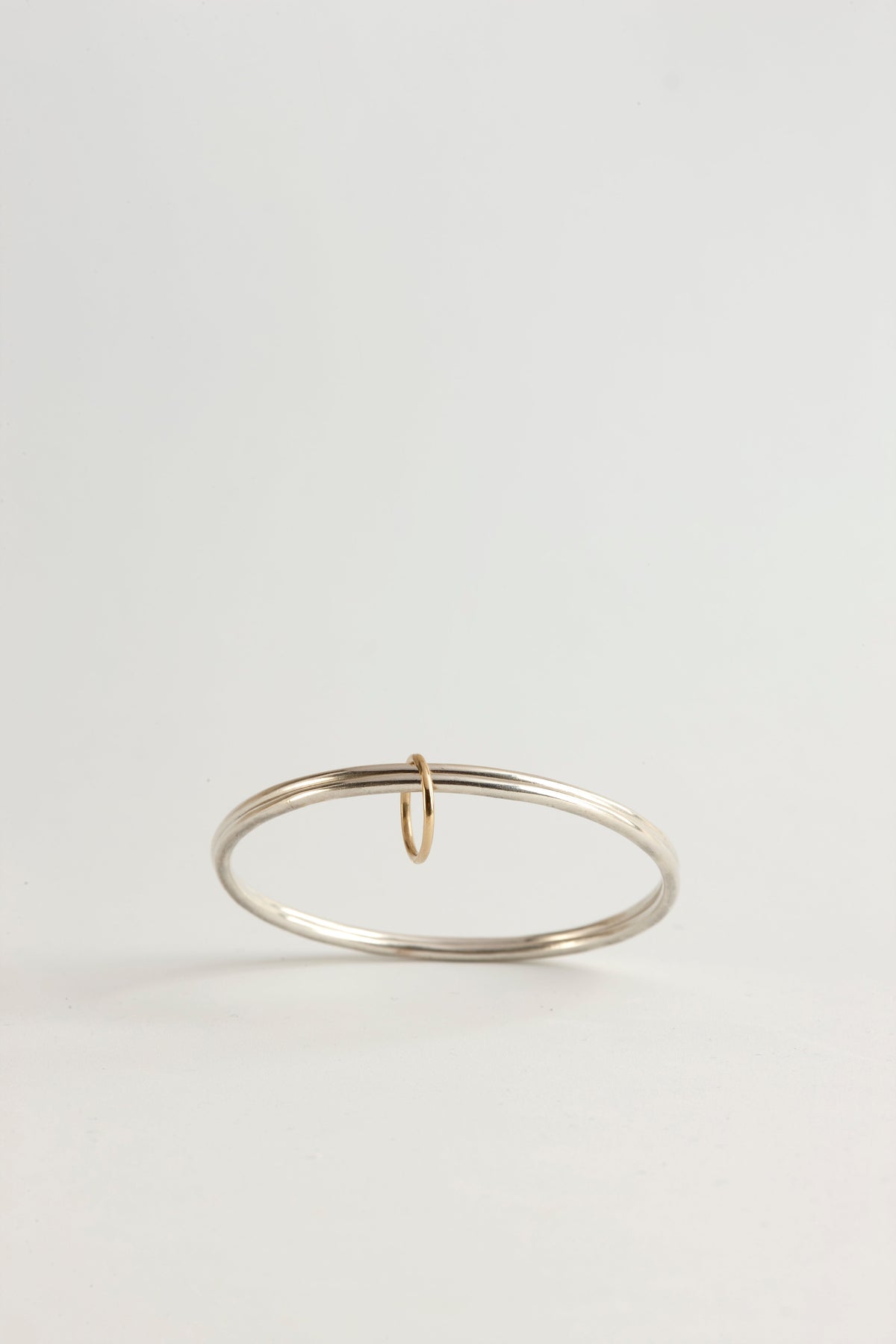 Cynthia Djurovic sterling silver bangle featuring a delicate 18k gold circle of life charm on a white background